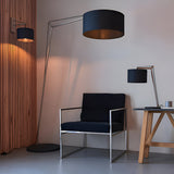 Carlfield Floor Lamp in nickel with black cotton drum shade on a cantilevered arm, shown beside a black armchair in a living room setting.