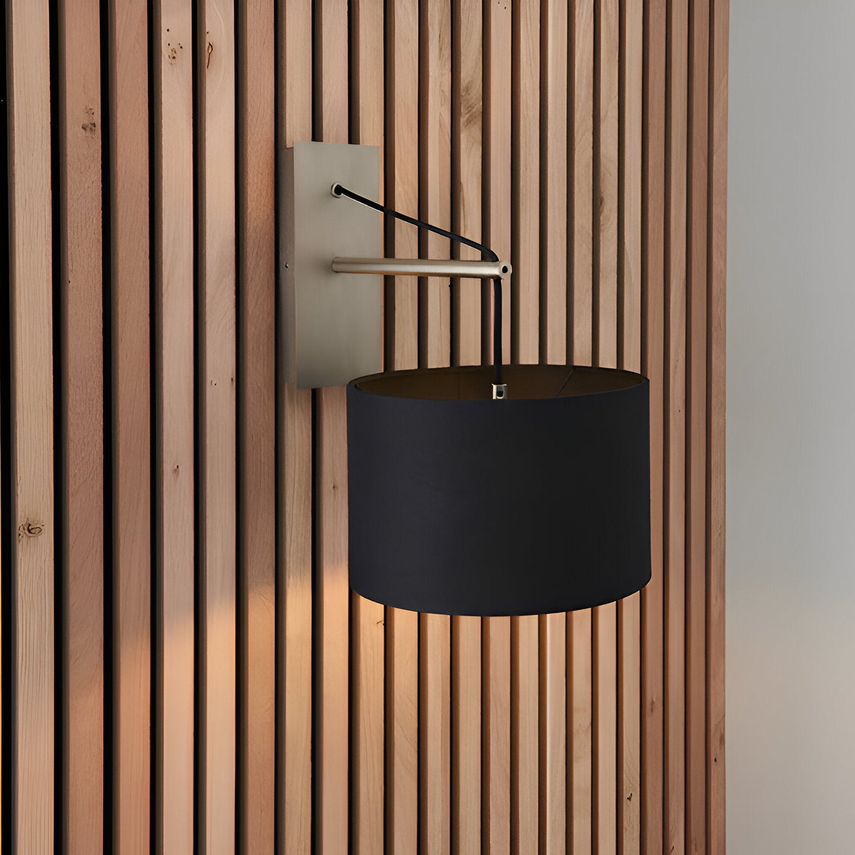 Carlfield Wall Light in nickel, cantilevered arm with black drum shade, mounted on wood slat panelling.