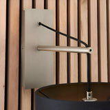 Carlfield Wall Light in Nickel, showing the matt nickel rectangular backplate, cantilevered stem, black fabric cord and shade, against a wooden slatted wall.
