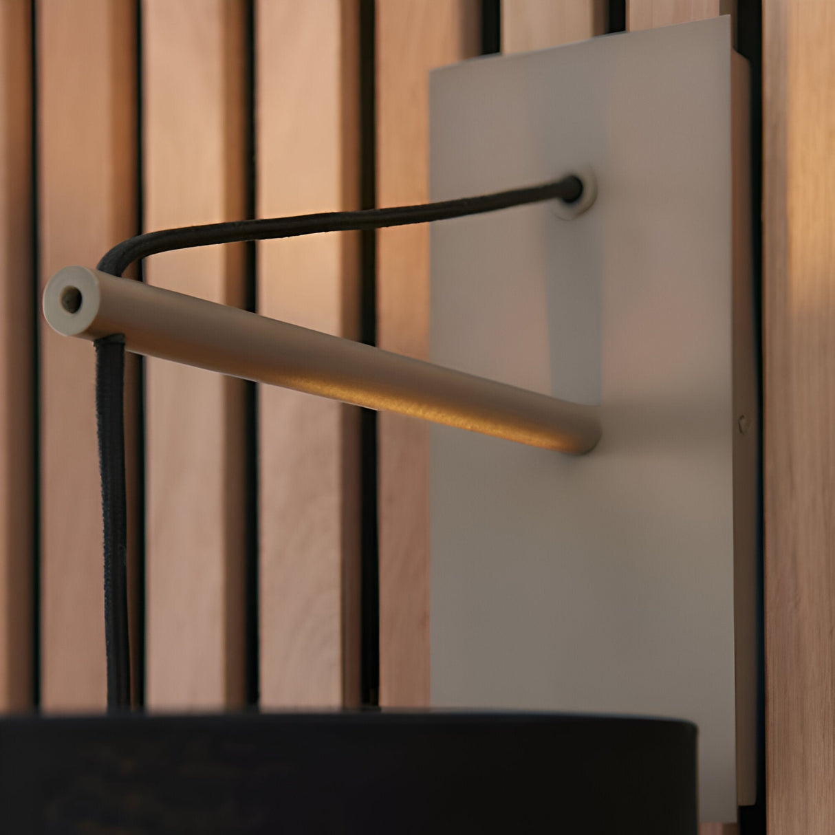 Carlfield Wall Light in Nickel, close-up of the matt nickel stem and black base with black fabric cotton shade against a wood slat background.
