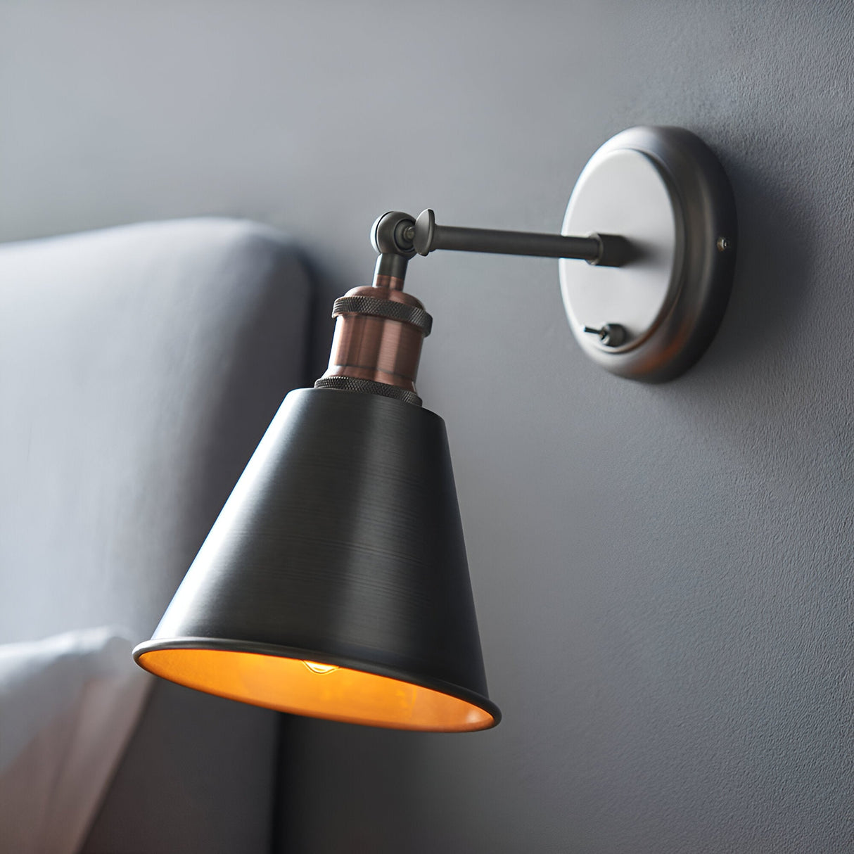 Endon Brackley industrial wall light with adjustable conical shade in aged pewter and copper, toggle switch on round backplate, mounted on grey wall.