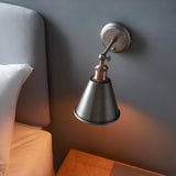 Endon Brackley wall light with adjustable conical shade in aged pewter and copper, mounted on grey bedroom wall beside upholstered headboard.