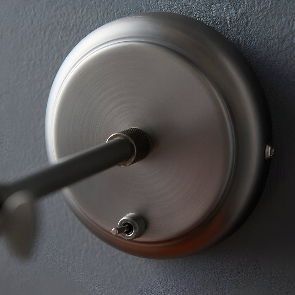Close-up of the Endon Brackley wall light backplate in aged pewter, showing the knurled arm fixing and toggle on/off switch against a grey wall.