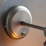 Close-up of the Brackley glass wall light's circular pewter backplate with knurled adjustable joint and extending arm, mounted on a textured wall.