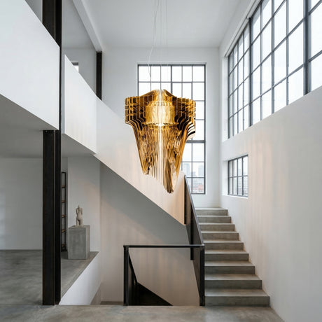 A modern, minimalist interior featuring concrete stairs, large industrial windows, white walls, and the Aeris 5 Light Large Chandelier in gold casting ambient light over the stairwell. Natural light flows through the space.