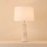 Orix Alabaster Pillar Table Lamp with tapered faceted white alabaster column, brushed brass collar, and soft white drum shade on a plain light background.
