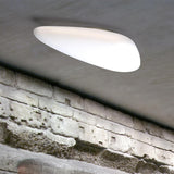 Stone LED Flush Ceiling Light in white, asymmetric pebble-shaped diffuser mounted on a grey ceiling above an exposed brick wall.
