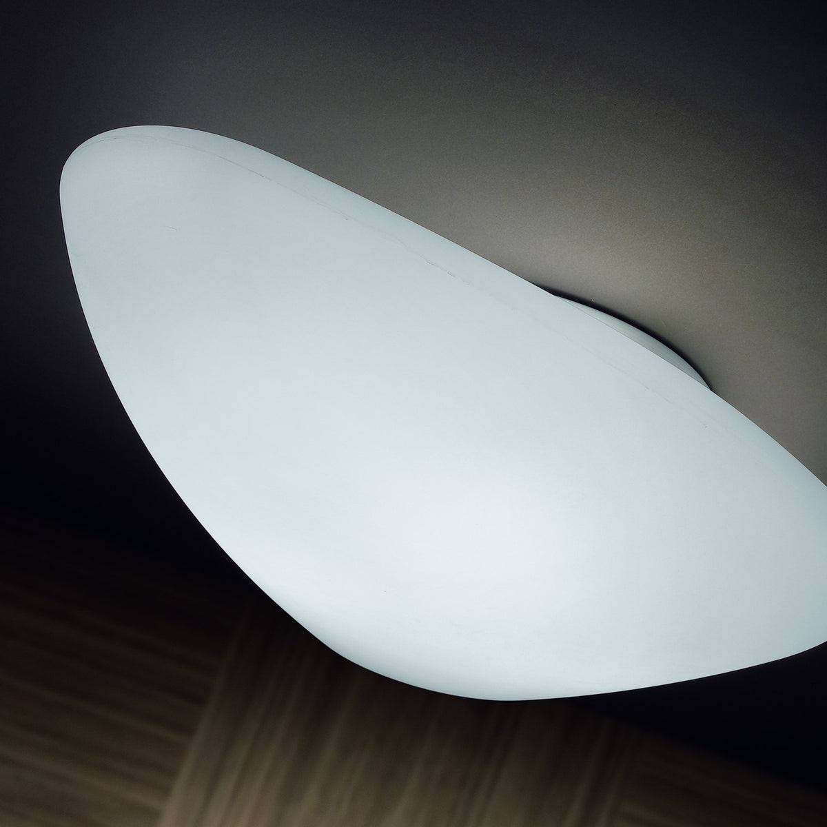 Stone LED Flush Ceiling Light in white, pebble-shaped diffuser mounted flush to a dark ceiling, glowing softly above a wooden floor.