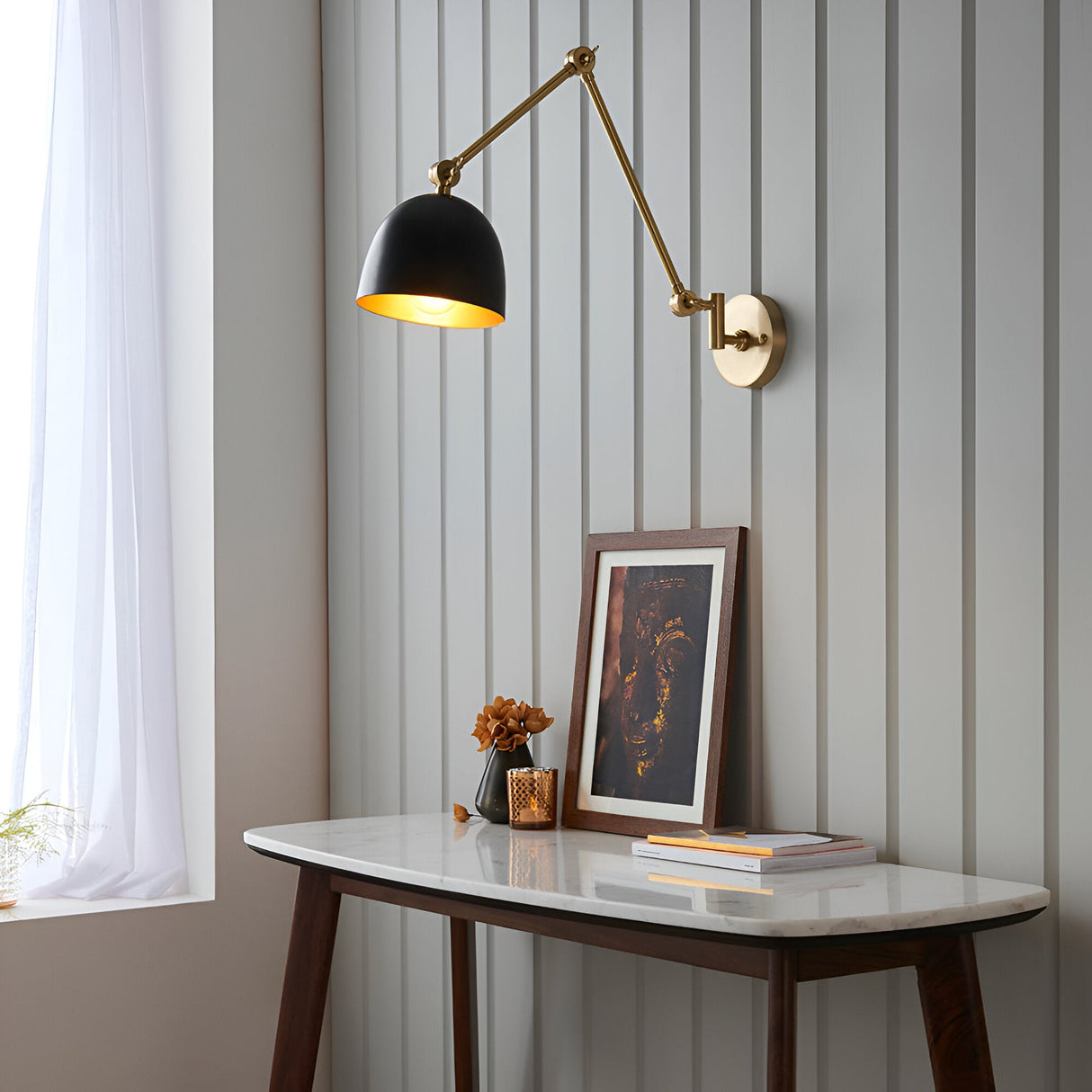 Caldhurst Wall Light in brass and black, adjustable dual-arm design with a matte black shade, shown above a console table in a living room setting.