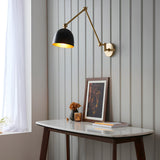 Caldhurst Wall Light in brass and black, adjustable dual-arm design with a matte black shade, shown above a console table in a living room setting.