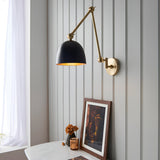 Caldhurst Wall Light in brass with a matt black shade and adjustable jointed arm, mounted on a grey panelled wall above a marble table.
