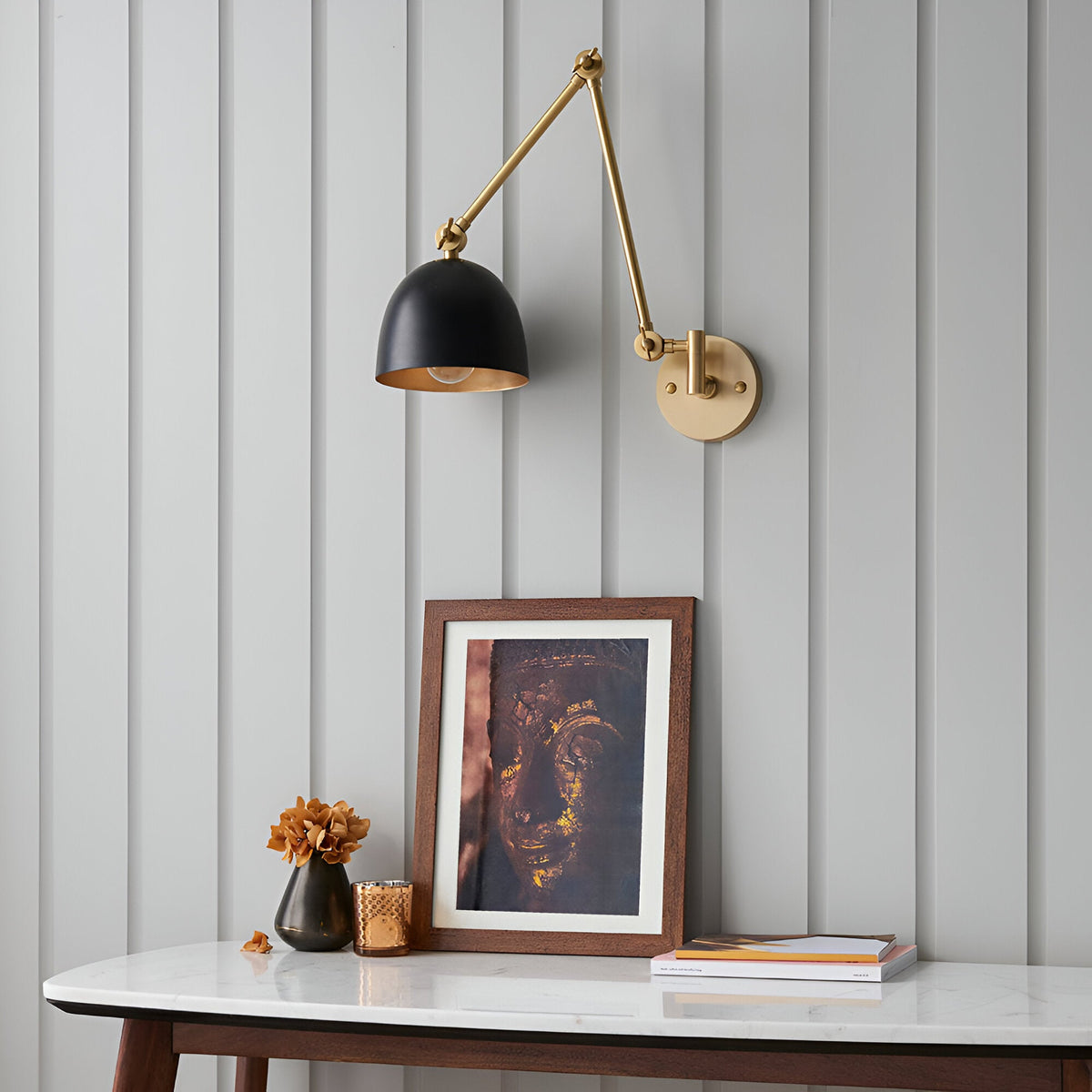 Caldhurst Wall Light in brass and black with adjustable jointed arm and dome shade, shown above a console table in a hallway setting.