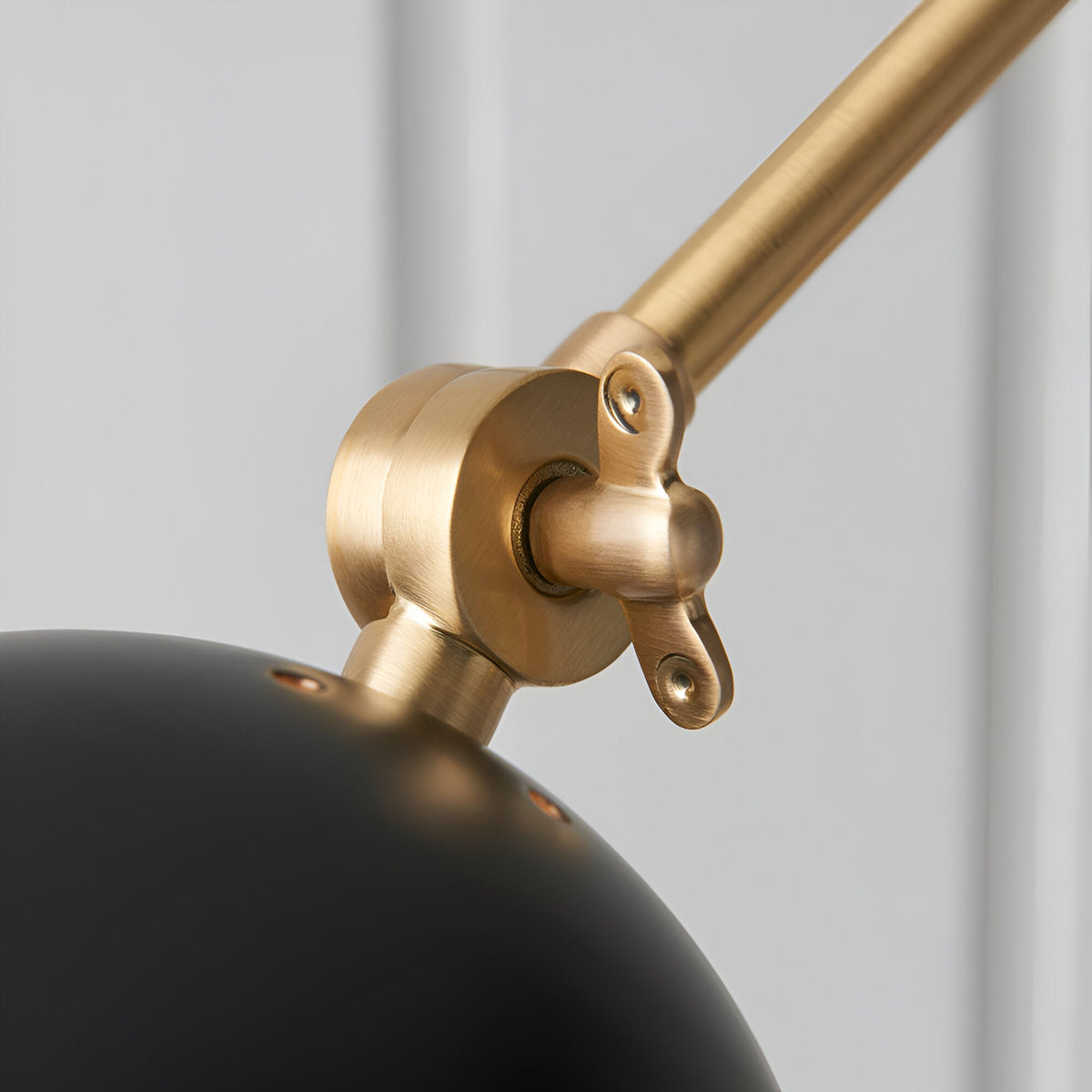 Close-up of the Caldhurst Wall Light's adjustable brass joint and arm, showing knurled metal detail above a matte black shade, on a plain grey background.