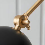 Close-up of the Caldhurst Wall Light's adjustable brass joint and arm, showing knurled metal detail above a matte black shade, on a plain grey background.