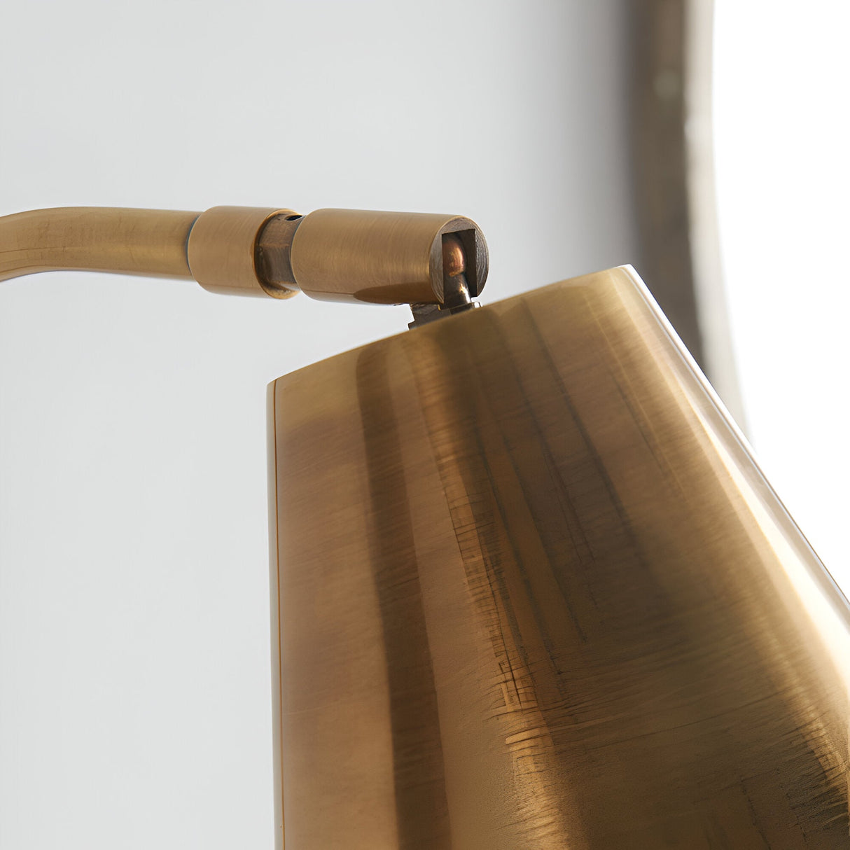 Close-up of the Chartmere Wall Light in antique brass, showing the adjustable angled shade and swivel joint on a curved metal arm.