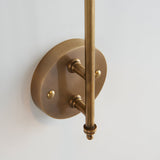 Chartmere Wall Light in antique brass, close-up of round wall plate, adjustable rod arm and decorative brass details on a white background.
