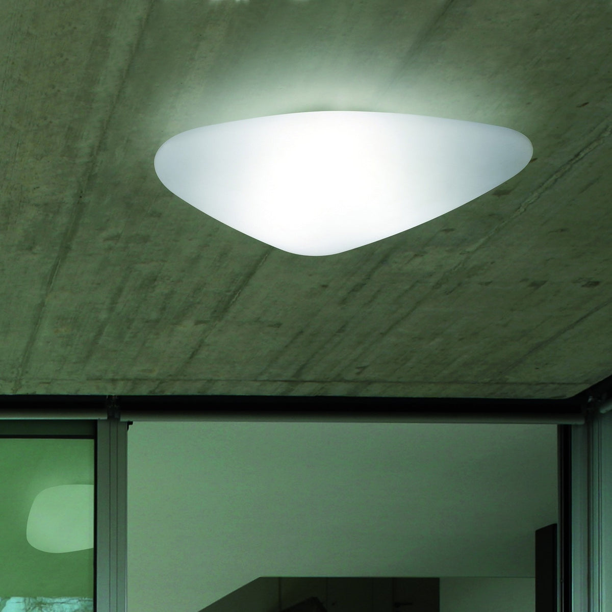 Stone LED Outdoor Flush Ceiling Light in white, pebble-shaped diffuser glowing on a concrete ceiling above a glazed interior doorway.