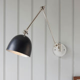 Endon Caldhurst adjustable wall light with polished nickel articulated arm and matt black dome shade, mounted on a grey panelled wall.