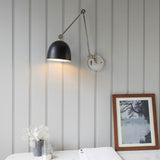 Endon Caldhurst adjustable wall light with polished nickel arm, matt black dome shade and round backplate, mounted on grey panelled wall above a marble surface.