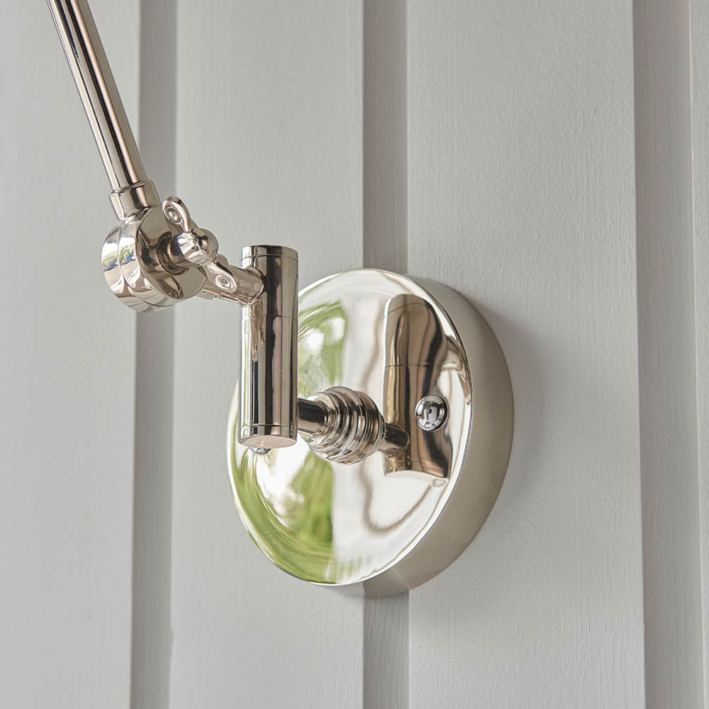 Endon Caldhurst wall light close-up showing polished nickel circular backplate with knurled fitting and jointed arm against a light grey panelled wall.