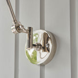 Endon Caldhurst wall light close-up showing polished nickel circular backplate with knurled fitting and jointed arm against a light grey panelled wall.