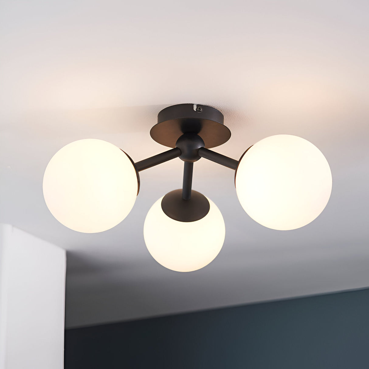 Endon Marden semi-flush bathroom ceiling light with three opal glass globes on matt black arms, mounted to a white ceiling in a modern interior.