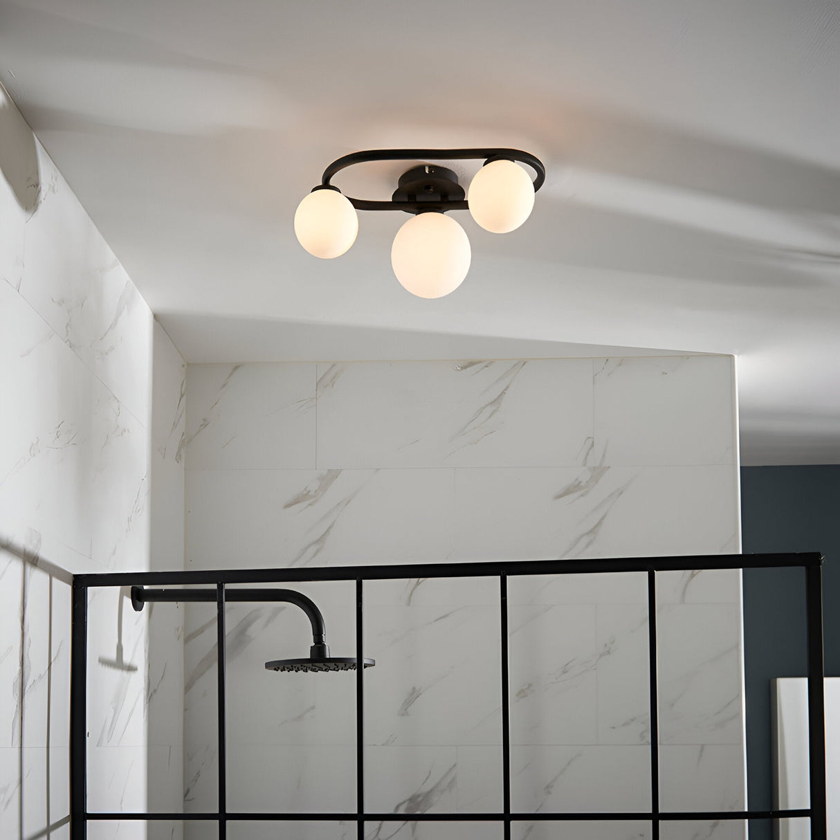 Endon Marden 3 light oval semi-flush bathroom ceiling light in matt black with opal glass globes, mounted above a walk-in shower with black framed screen.
