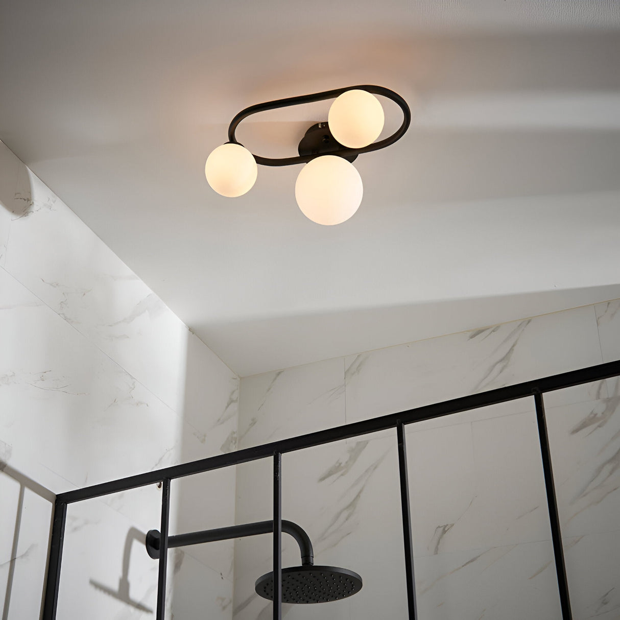 Endon Marden semi-flush bathroom ceiling light in matt black with three opal glass globes set in an oval steel frame, above a marble-tiled shower.
