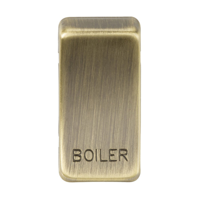 The product is a "Marked BOILER" switch cover in Antique Brass, featuring the word 'BOILER' engraved on it. It has a brushed metal texture that provides a vintage or industrial look. This rectangular cover with rounded edges gives off a classic rocker switch vibe for an elegant and timeless appeal.