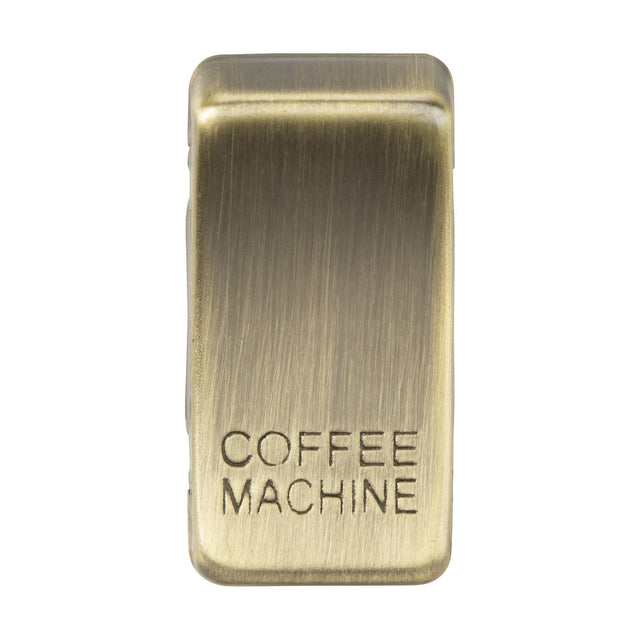 A close-up of the Switch Cover "Marked COFFEE MACHINE" in Antique Brass showcases its vintage charm with a brushed texture. The rocker covers are set to off, standing out against a white background.