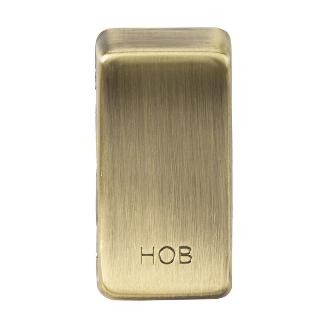 A rectangular object in antique brass metal, featuring rounded edges and engraved with the text "HOB," evokes the classic appearance of a rocker cover. This is the Switch Cover "Marked HOB" - Antique Brass.
