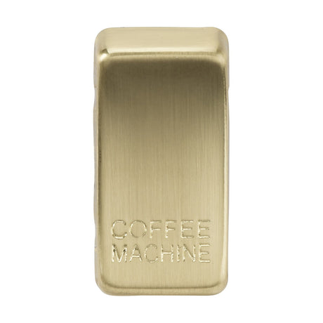 A brushed brass metallic switch cover marked with "COFFEE MACHINE," featuring a refined texture and a rectangular shape with slightly rounded edges.