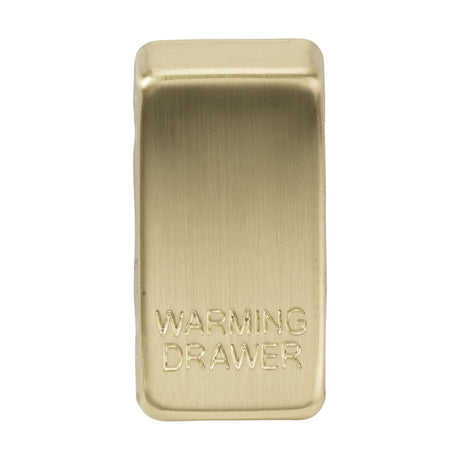 A rectangular brushed brass switch cover, similar to those found on high-end appliances such as dishwashers, is engraved with the words "WARMING DRAWER" on its front. Its smooth, rounded edges and brushed finish lend it an elegant appearance.