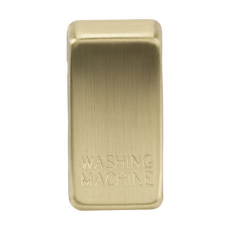 Close-up of a metallic rectangular object with ABS construction and a brushed brass finish. The words WASHING MACHINE are engraved on it.