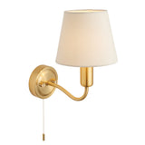 Endon Bevton bathroom wall light with a curved satin brass arm, ivory fabric tapered shade, and pull cord switch, shown on a plain white background.
