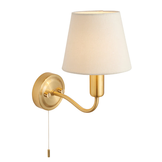 Endon Bevton bathroom wall light with a curved satin brass arm, ivory fabric tapered shade, and pull cord switch, shown on a plain white background.