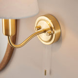 Close-up of Endon Bevton bathroom wall light showing satin brass backplate, curved arm and pull cord switch mounted on a neutral wall.