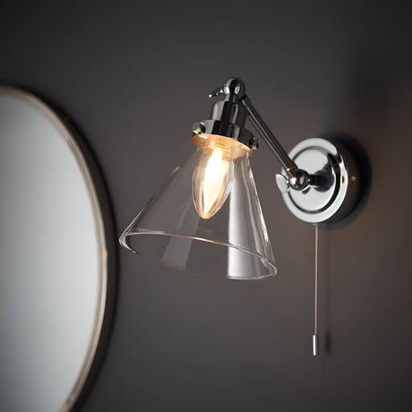 Endon Brackwood bathroom wall light in chrome with clear glass conical shade, adjustable head and pull cord switch, mounted beside a round mirror.