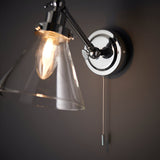 Endon Brackwood chrome bathroom wall light with clear glass conical shade, adjustable arm, and pull cord switch mounted on a grey wall.