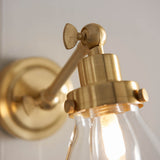 Close-up of Endon Brackwood brass bathroom wall light showing the adjustable pivot head, round wall plate, and clear glass shade with G9 bulb lit inside.