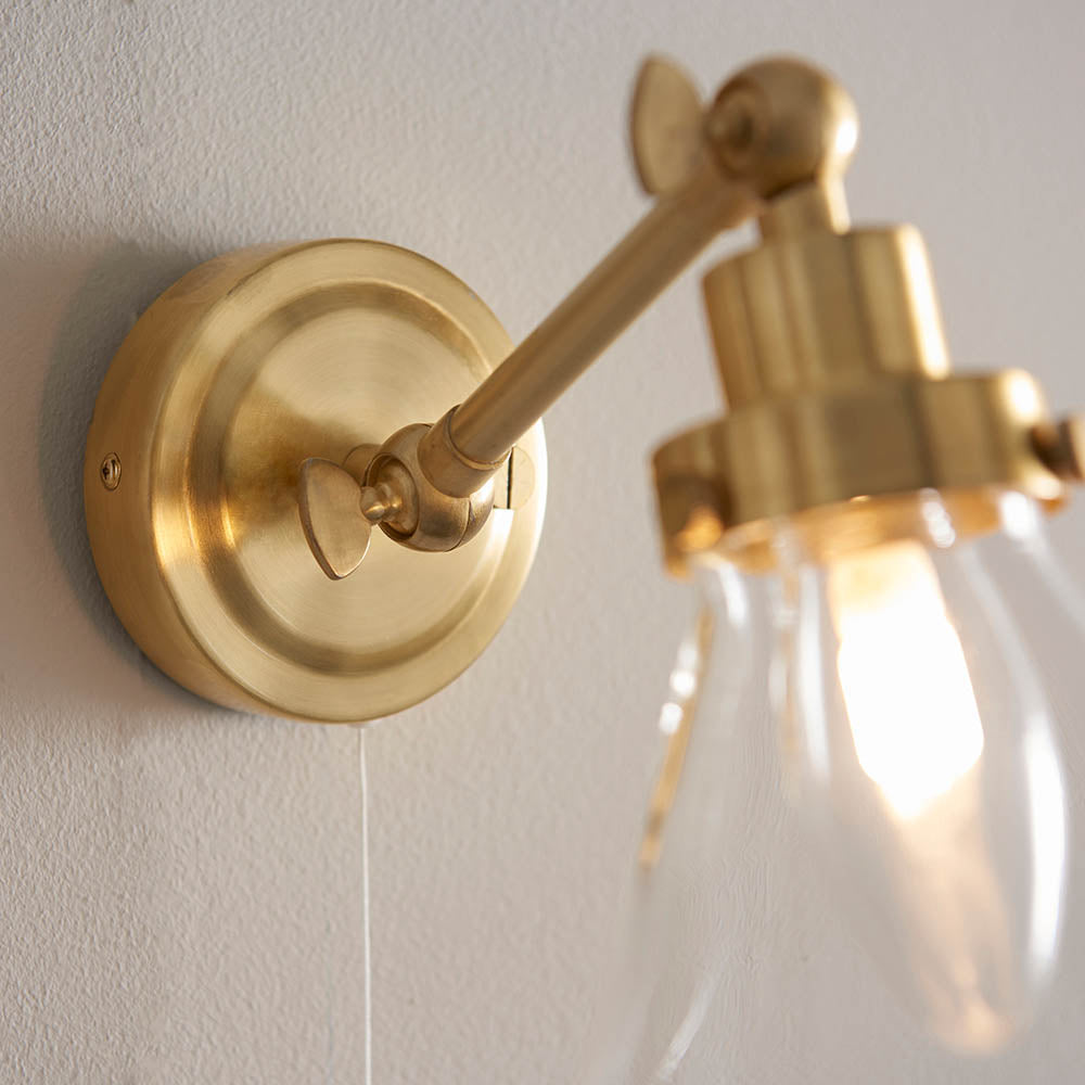 Endon Brackwood bathroom wall light in brass, close-up of the adjustable arm, round wall plate and clear glass shade with illuminated G9 bulb.