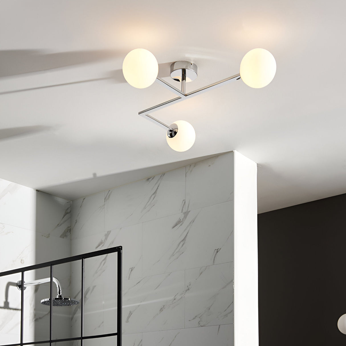 Kelham 3 Light Semi-Flush Bathroom Ceiling Light in chrome with three round opal glass globes on angled arms, installed above a marble-tiled shower area.