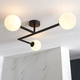 Endon Kelham 3 light semi-flush bathroom ceiling light in black, with three white glass globe shades on angular arms fixed to a white ceiling.