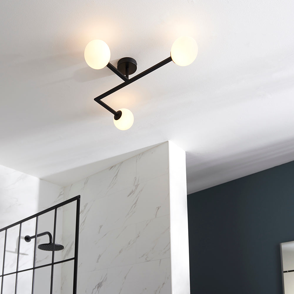 Endon Kelham 3 light semi-flush bathroom ceiling light in black with angular arms and three white glass globes, mounted above a marble-tiled shower.