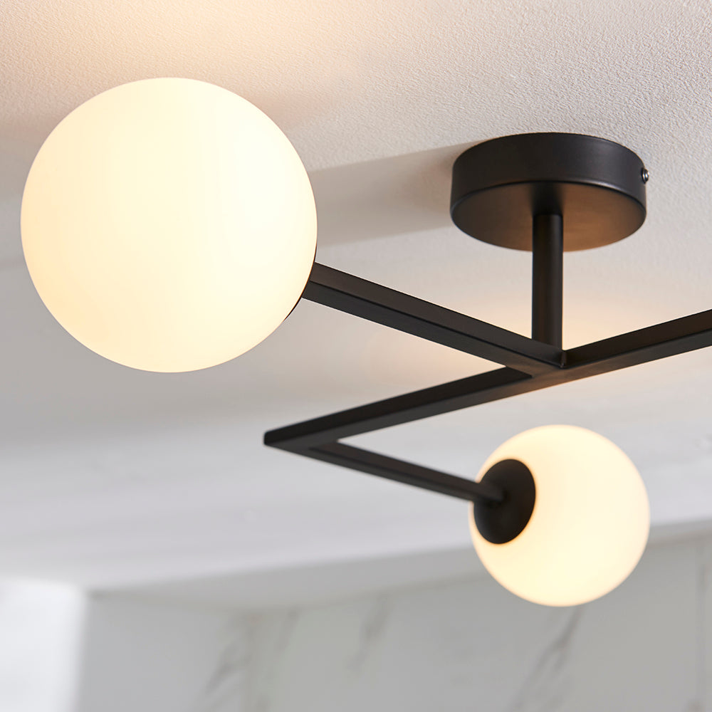 Endon Kelham semi-flush bathroom ceiling light in black with angular arms and opal glass globe shades, mounted to a white ceiling.
