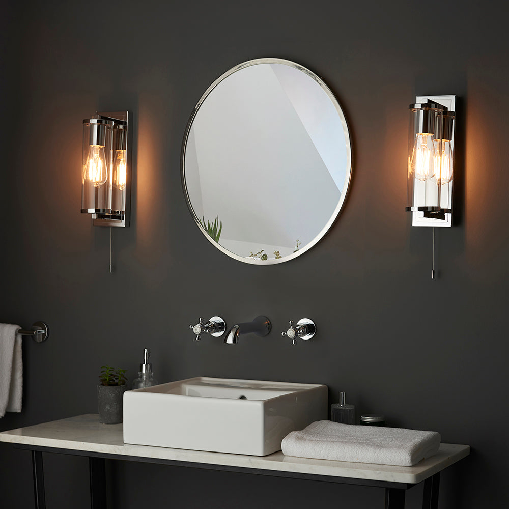 Endon Cranfield chrome bathroom wall lights with tubular clear glass shades and E27 filament bulbs, mounted either side of a round mirror above a basin.