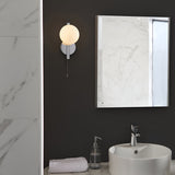 Endon Kelham bathroom wall light in chrome with opal glass sphere and pull cord, mounted on a dark wall beside a marble-framed mirror above a basin.