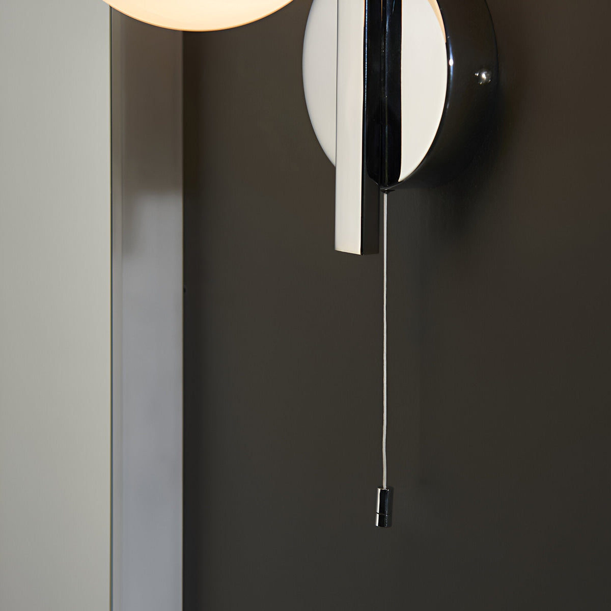 Endon Kelham bathroom wall light in chrome, close-up of the circular backplate and pull-cord switch mounted on a dark wall.