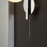 Endon Kelham bathroom wall light in chrome, close-up of the circular backplate and pull-cord switch mounted on a dark wall.