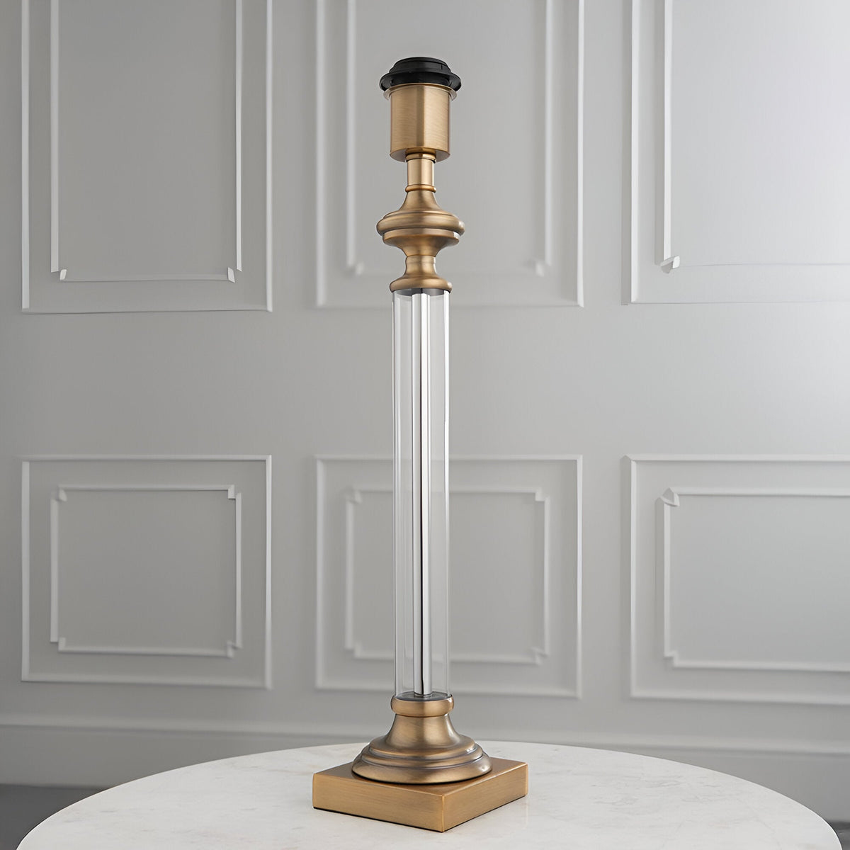 Endon Aldmont table lamp base with clear glass column and antique brass detailing on a square base, set on a marble table against a panelled wall.